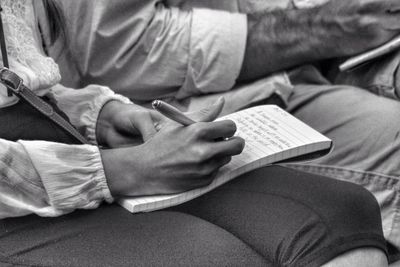 Midsection of woman sitting by man writing on book