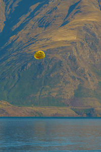 Distant view of person parasailing over sea against mountain