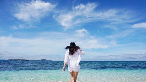 Rear view of woman standing at beach against sky