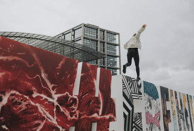 Low angle view of woman balancing on graffiti wall against sky