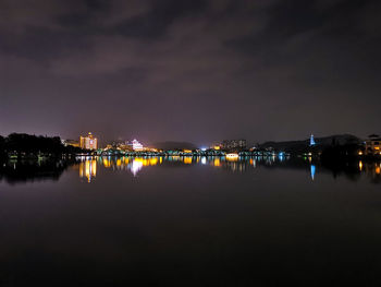 Illuminated city by river against sky at night