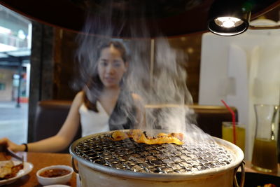 Woman looking at food on barbecue grill while sitting in restaurant