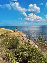 Rear view of woman  sitting on rock by sea against sky