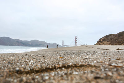 People fishing at beach with golden gate bridge in background against sky