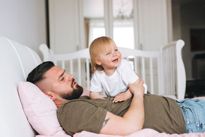 Young happy family with father and daughter baby girl on bed in cozy home