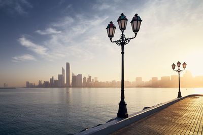 Street light by sea against buildings in city against sky