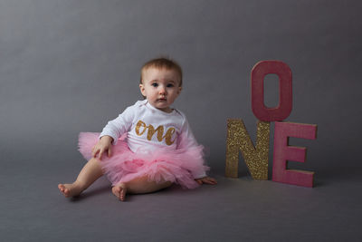 Baby girl sitting with sparkling text over gray background