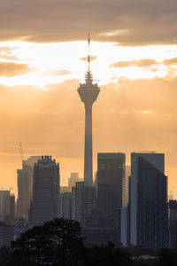 Trees and buildings against cloudy sky during sunset