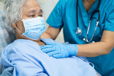 Midsection of doctor examining patient wearing ask at hospital