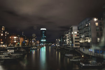 Illuminated buildings by river against sky at night