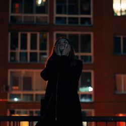 Sad woman standing against building at night