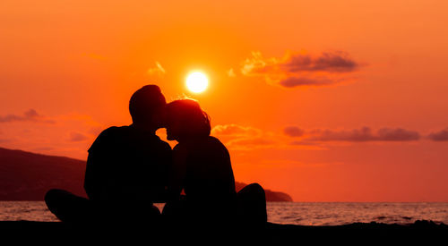 Couple sitting at beach, silhouette in sunset, love and friendship.