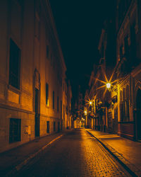 Empty road along illuminated buildings at night