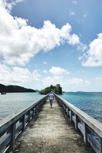 Rear view of man standing on railing by sea against sky