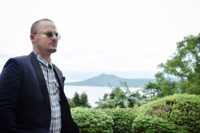 Young man wearing sunglasses standing on mountain against sky