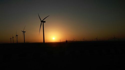 Silhouette wind turbines on field against sky during sunset