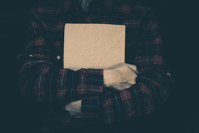 Midsection of man holding paper against black background