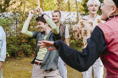 Happy non-binary person dancing amidts lgbtq friends during party in back yard