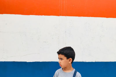 Thoughtful boy standing against painted wall