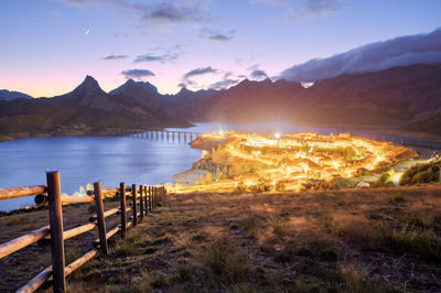 Breathtaking scenery of small town located near river surrounded by massive rocky mountains under scenic sunset sky in riano