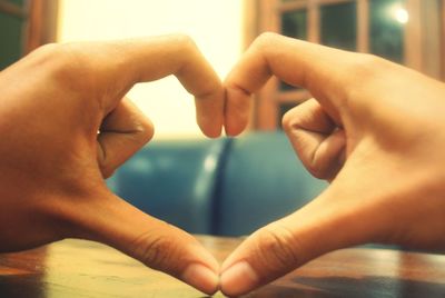 Cropped image of hands making heart shape on table