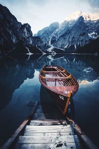 Boat moored on calm lake against mountain during winter