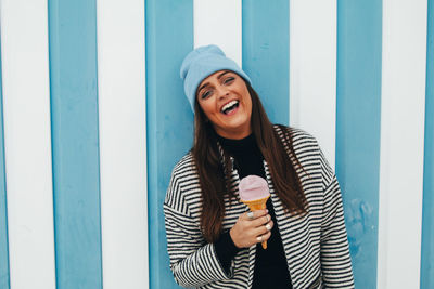 Portrait of cheerful woman having ice cream cone by striped wall