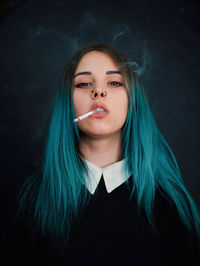 Portrait of hipster smoking cigarette against black background