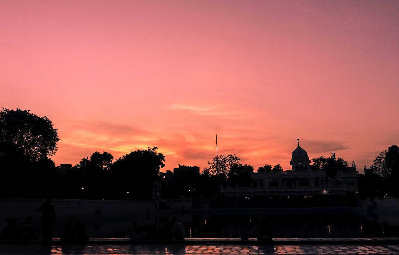 SILHOUETTE TREES BY BUILDING AGAINST ORANGE SKY