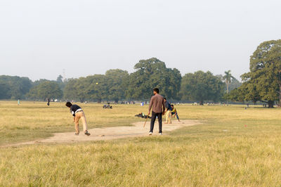 Rear view of men walking on field against sky
