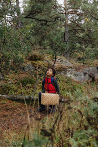 Thoughtful boy with basket looking up while sitting in forest