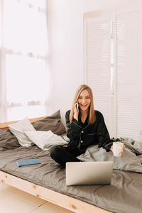 Young woman using mobile phone while sitting on bed