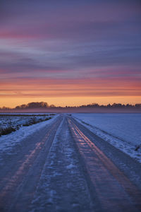 Surface level of snowy field against sky during sunset