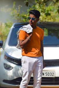 Portrait of young man standing against car