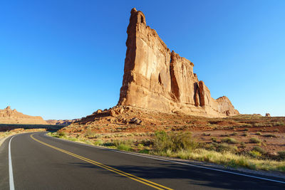Road by rock formation against clear blue sky