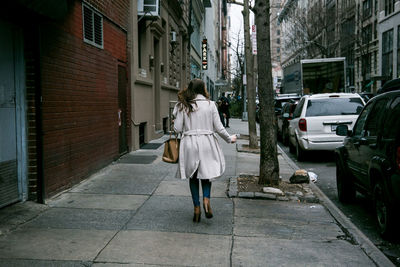 Full length rear view of woman walking on sidewalk in city