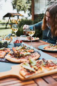 Family and friends having meal - pizza, salads, fruits and drinking white wine during summer picnic