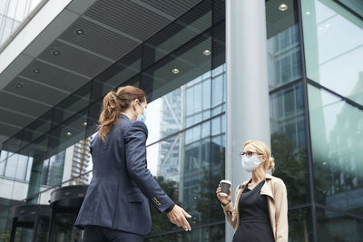 Business people wearing face mask talking while standing against office building