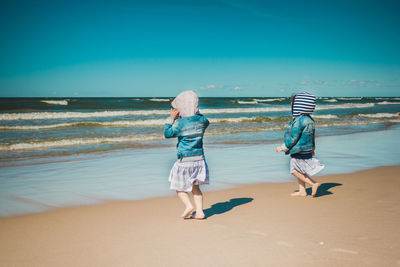 Full length of siblings walking at beach against sea and sky