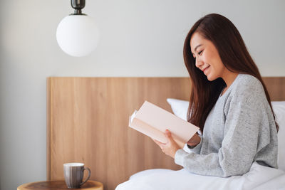 Smiling woman reading book sitting on bed