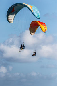 Low angle view of people paragliding against sky