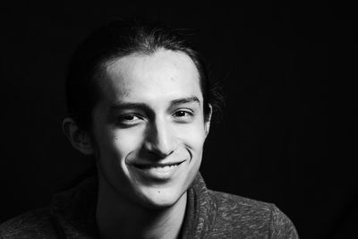 Portrait of smiling young woman against black background