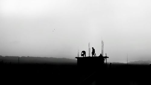 Silhouette people on field against sky during foggy weather