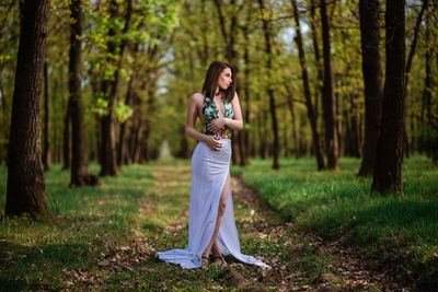 Woman standing by tree trunk in forest