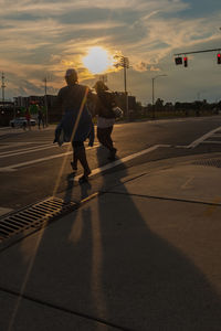 People walking on road in city against sunset sky