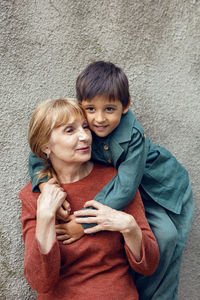 Child boy hugs his grandmother an elderly woman on the street against a gray wall