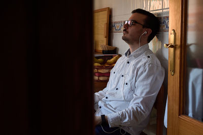 A young man listens to music with his headphones sitting at home