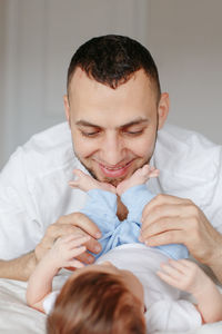 Father playing with baby daughter lying on bed at home