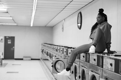 Full length of woman sitting at laundry room