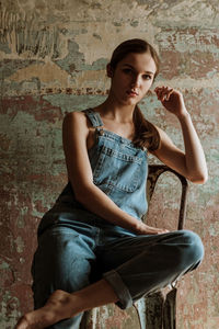 Portrait of young woman sitting against wall